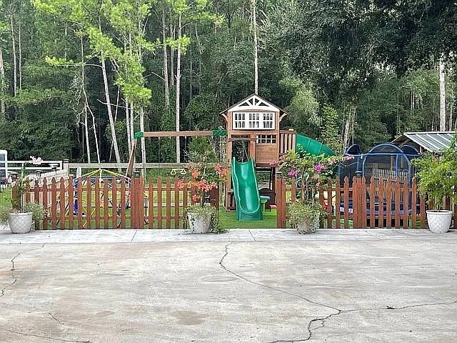 A wooden playset with a green slide sits behind a brown fence in a backyard — 9068 131ST LOOP, LIVE OAK, FL
