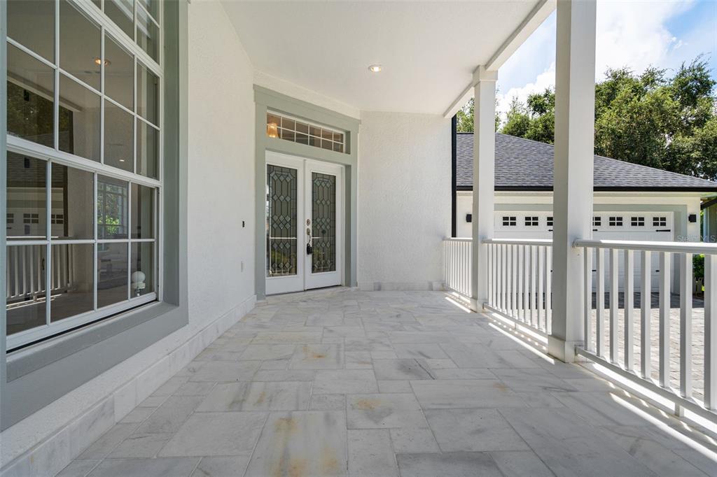A covered front porch with stone flooring, white railings, and double glass-paneled entry doors — 5927 CAYMUS LOOP, WINDERMERE, FL