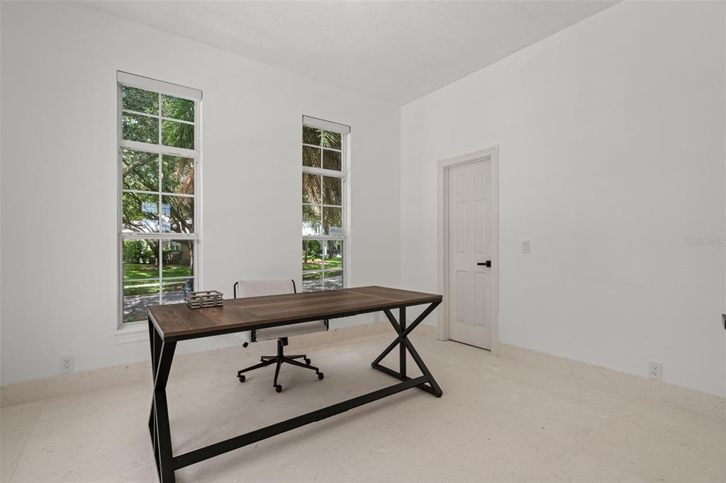 A home office features a wooden desk, a rolling chair, two tall windows, and tile flooring — 5927 CAYMUS LOOP, WINDERMERE, FL