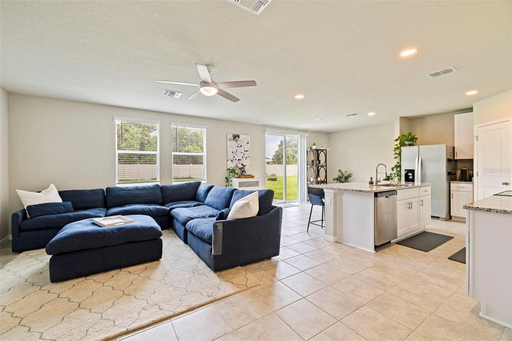 An open-concept living room and kitchen featuring a blue sectional sofa and a kitchen island — 7117 BOGGY CREEK PLACE, PARRISH, FL