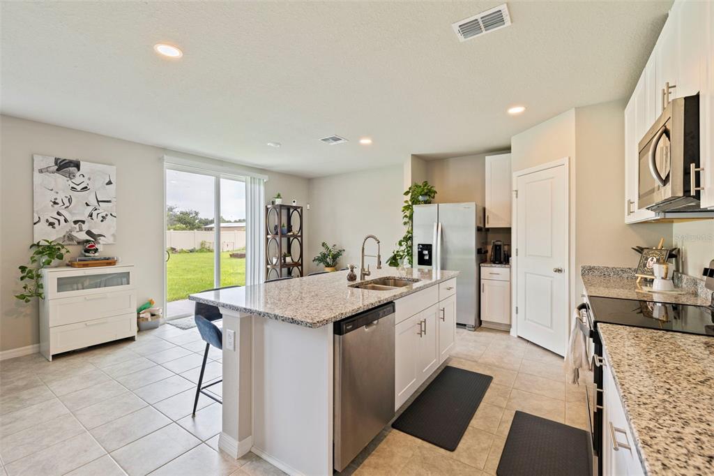 A kitchen with granite countertops, white cabinets, stainless steel appliances, and a sliding glass door — 7117 BOGGY CREEK PLACE, PARRISH, FL