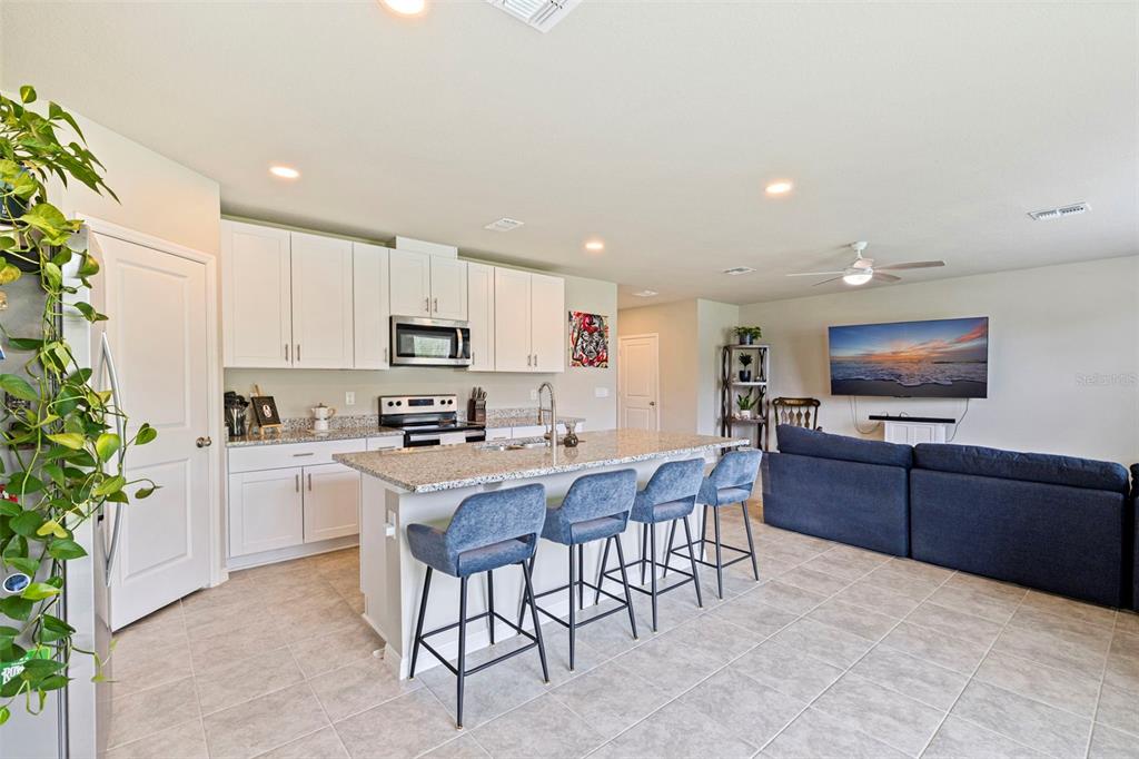 An open-concept kitchen with white cabinets, granite countertops, and an island with four barstools — 7117 BOGGY CREEK PLACE, PARRISH, FL