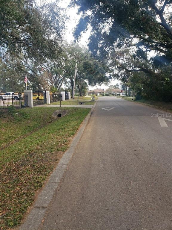 A paved road leads toward a gated entrance with large trees and a grassy ditch — 4217 W JACKSON STREET, ORLANDO, FL