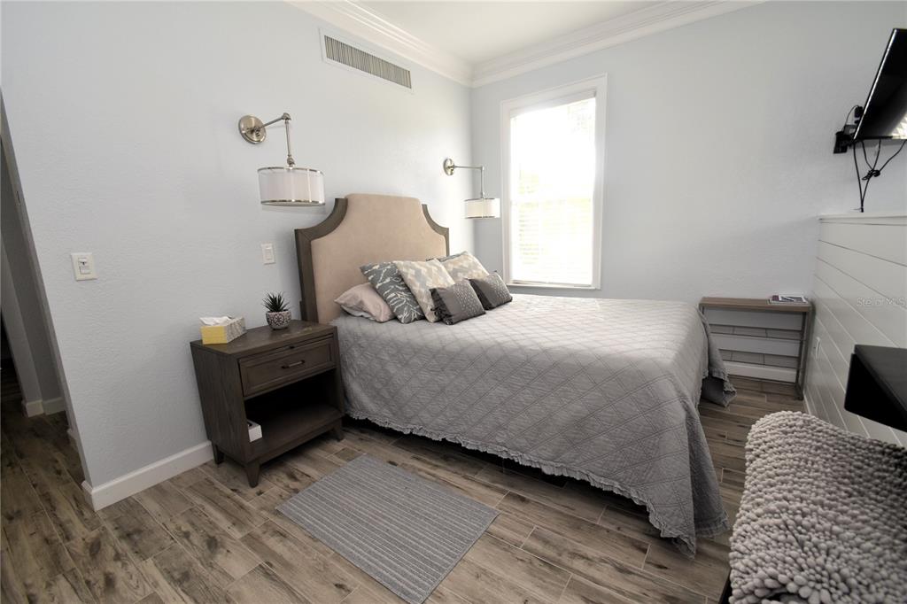A bedroom features a bed with a beige headboard, two wall lamps, and wood-look flooring — 51 MAC EWEN DRIVE UNIT 1, OSPREY, FL