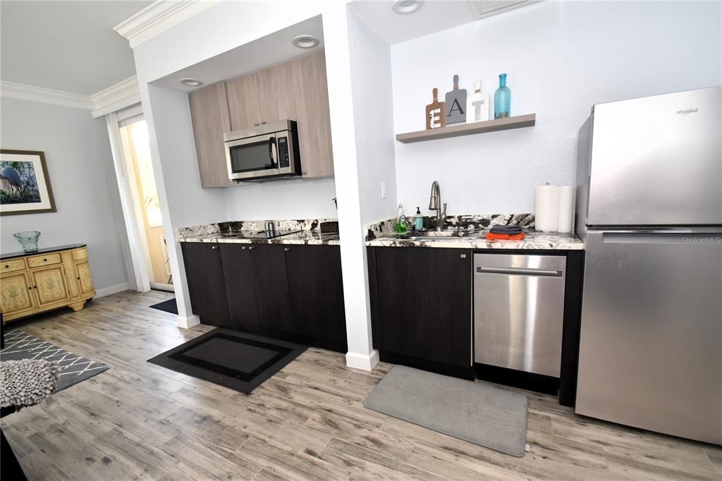 A kitchen features dark lower cabinets, light wood upper cabinets, granite countertops, and stainless appliances — 51 MAC EWEN DRIVE UNIT 1, OSPREY, FL
