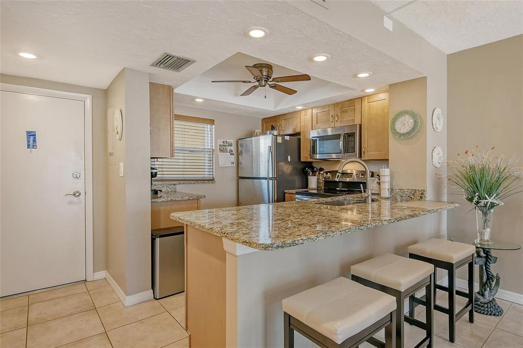 A kitchen features granite countertops, light wood cabinets, stainless steel appliances, and a breakfast bar — 1300 N PORTOFINO DRIVE UNIT 305, SARASOTA, FL