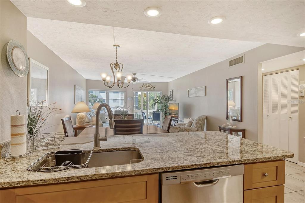A kitchen island with a granite countertop and stainless steel sink overlooks a living area — 1300 N PORTOFINO DRIVE UNIT 305, SARASOTA, FL