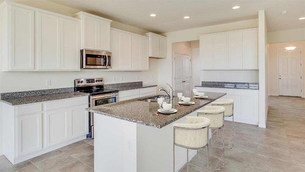 A kitchen features white cabinets, granite countertops, a center island with seating, and tile flooring — 35616 LOWERY TRAIL, ZEPHYRHILLS, FL