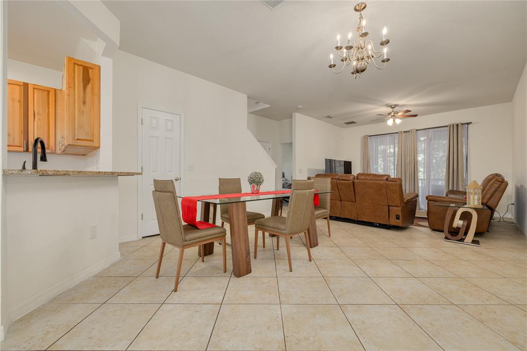 An open-concept dining and living area features tile flooring, a glass dining table, and chandelier — 13204 SAN BLAS LOOP, LARGO, FL