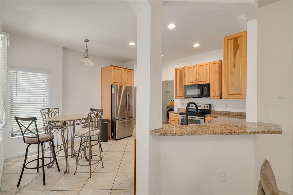A kitchen with light wood cabinets, granite countertops, and a small dining area with chairs — 13204 SAN BLAS LOOP, LARGO, FL