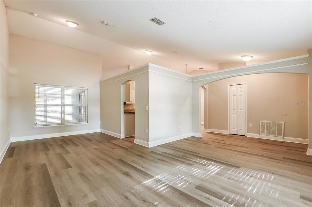 An empty living room features light wood-look flooring, vaulted ceilings, and an arched wall opening — 2823 ARBOUR TRAIL COURT, DELTONA, FL