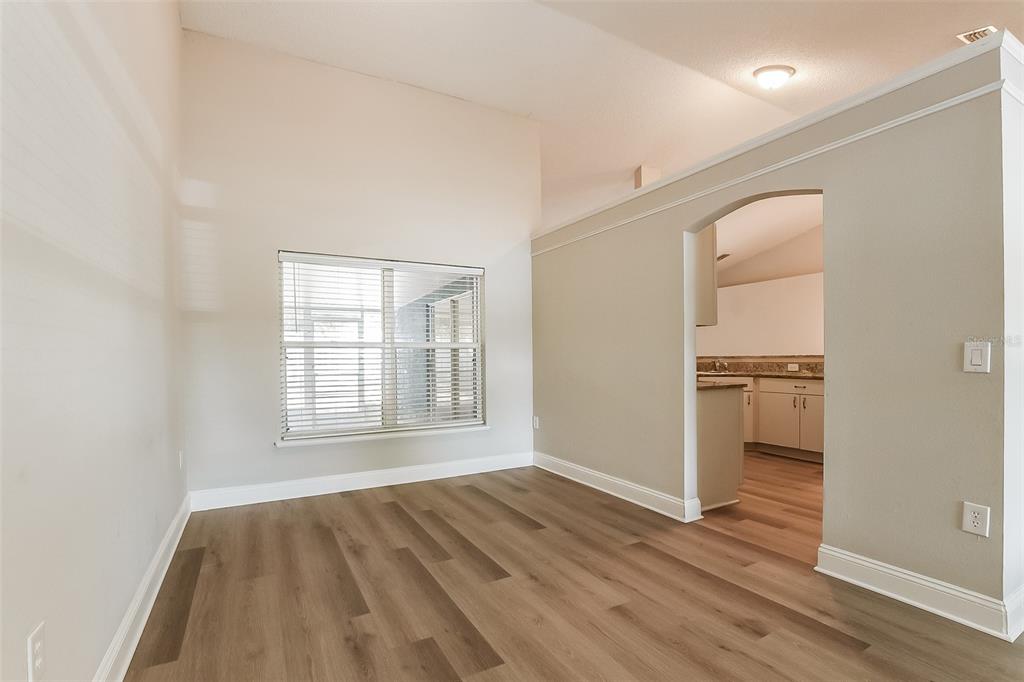 An empty room with wood-look flooring, a large window, and an arched entryway to a kitchen — 2823 ARBOUR TRAIL COURT, DELTONA, FL
