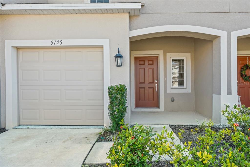 The exterior of a townhouse features a beige garage, a brown front door, and landscaping — 5725 HAVEN TERRACE, NOKOMIS, FL