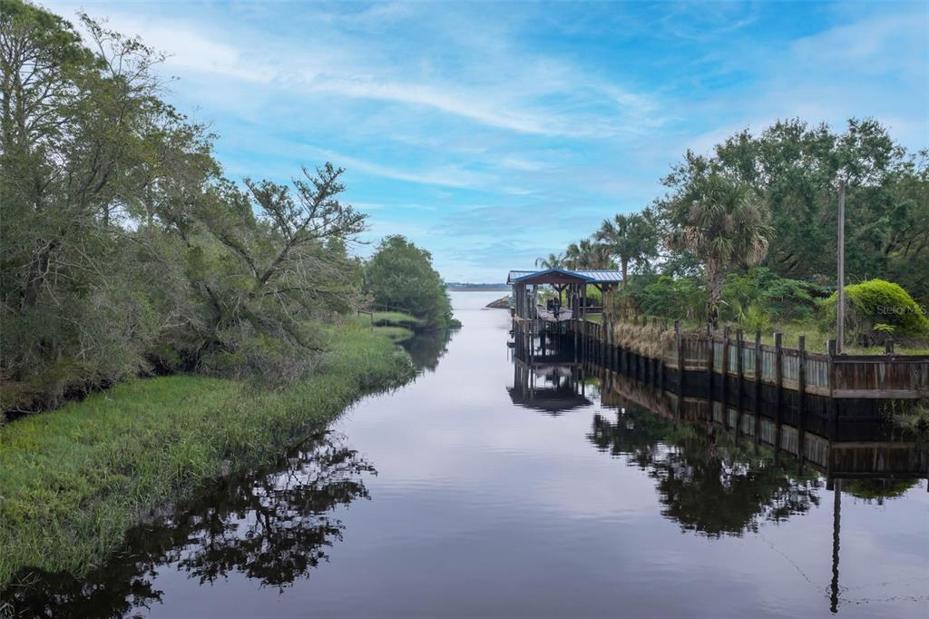 A canal leads to open water past a wooden boat dock and lush green trees — 16229 SHELLCRACKER ROAD, JACKSONVILLE, FL
