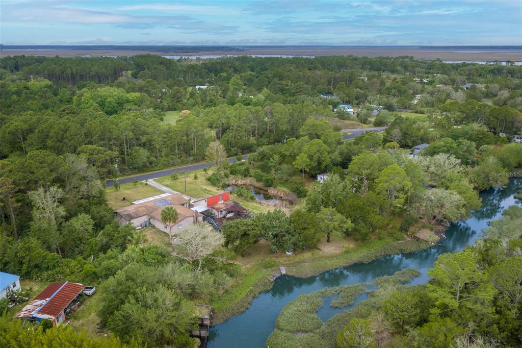 An aerial view shows a house with a red section situated near a winding creek — 16229 SHELLCRACKER ROAD, JACKSONVILLE, FL