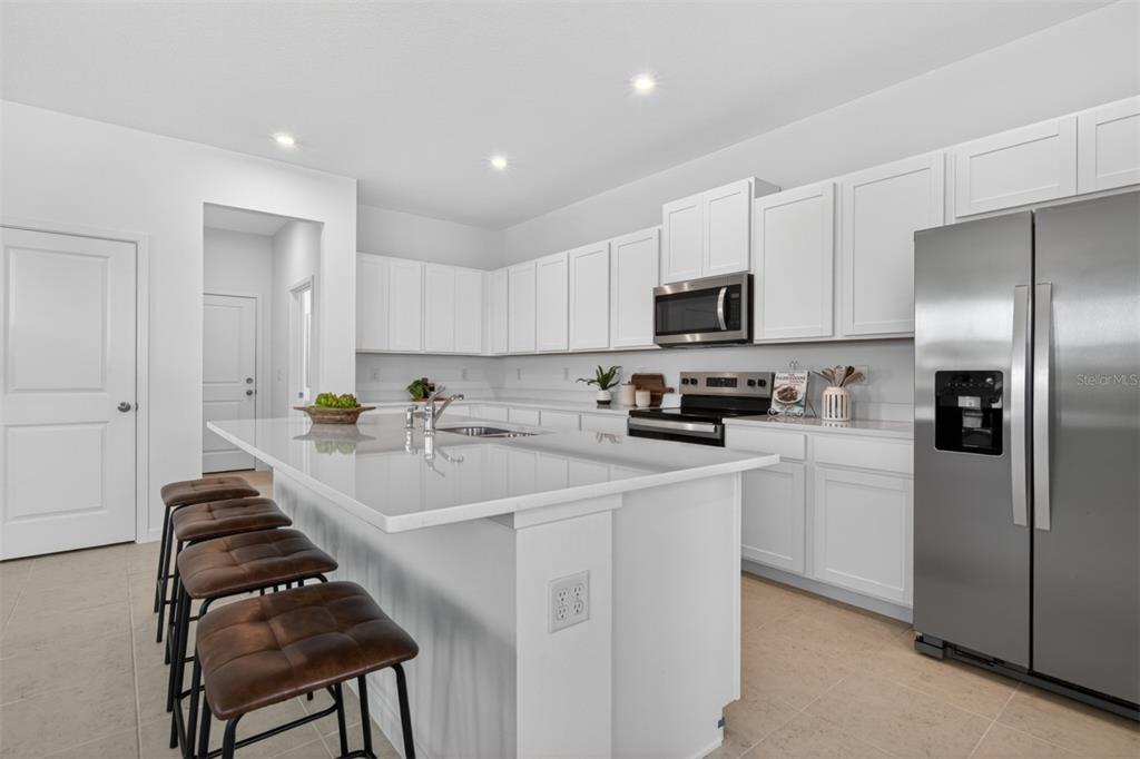 A modern kitchen features white cabinetry, stainless steel appliances, and a large island with seating — 13636 SEAGRASS AVENUE, ORLANDO, FL