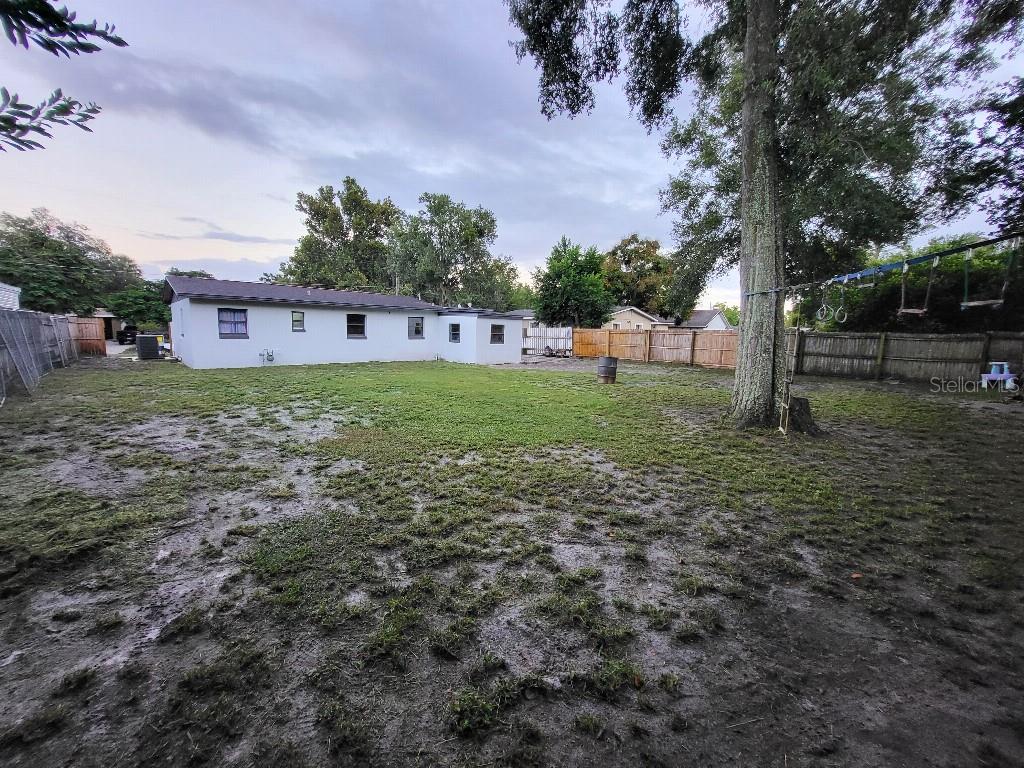 A backyard features a white house, a large tree, a wooden fence, and patchy grass — 995 EMERALD DRIVE, MOUNT DORA, FL