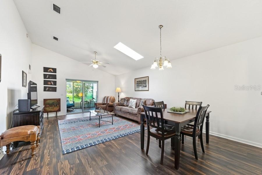 A living and dining room with wood-look flooring, a vaulted ceiling, and a sliding glass door — 2038 NW 50TH AVENUE, OCALA, FL