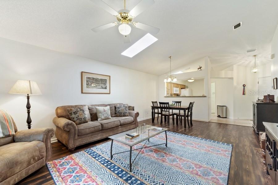 A living room with wood-look flooring, a patterned area rug, and an adjacent dining area — 2038 NW 50TH AVENUE, OCALA, FL