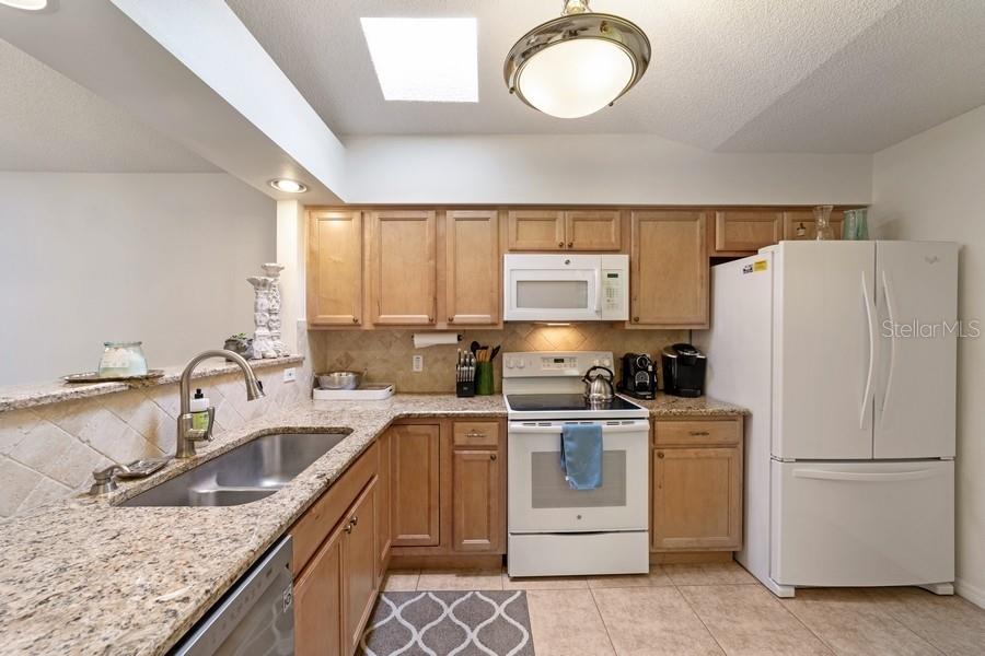 A kitchen features light wood cabinets, granite countertops, white appliances, and a skylight — 2038 NW 50TH AVENUE, OCALA, FL