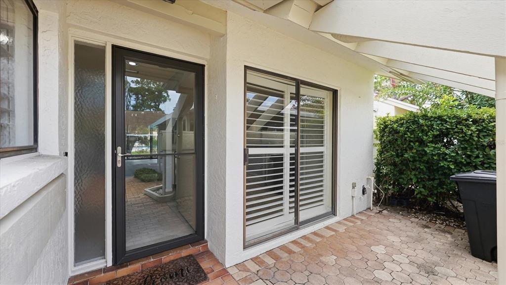 A paved patio features a glass storm door, a sliding glass door, and a trash bin — 5350 MYRTLE UNIT 48, SARASOTA, FL