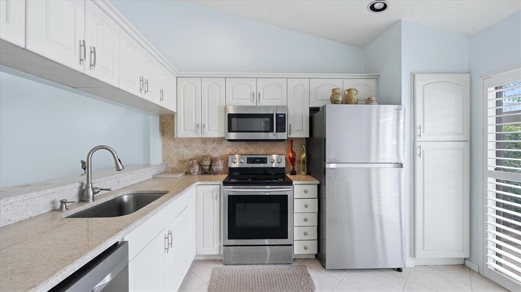 A kitchen features white cabinetry, stainless steel appliances, and light-colored granite countertops — 5350 MYRTLE UNIT 48, SARASOTA, FL