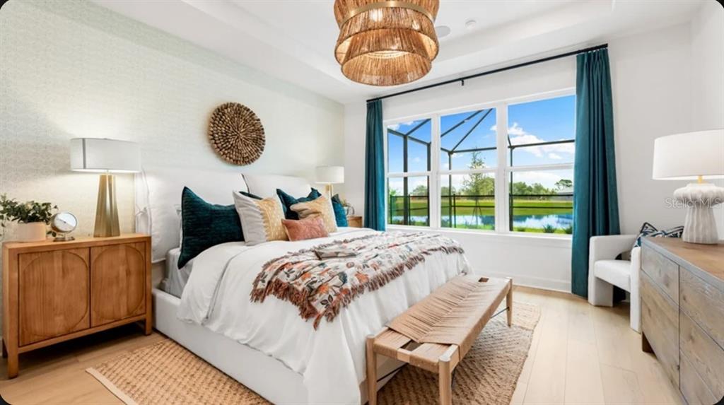 A bedroom features a white bed, a woven bench, teal curtains, and a view of water — 13906 FLETCHER DRIVE, PALMETTO, FL