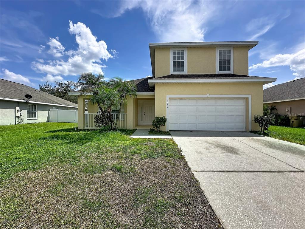 A two-story yellow house with a white garage door and a front porch — 3066 EAGLE CROSSING DR, KISSIMMEE, FL