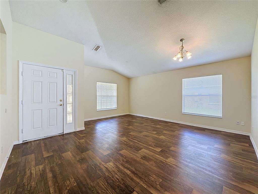 An empty living room features light-colored walls, a vaulted ceiling, and dark wood-look flooring — 3066 EAGLE CROSSING DR, KISSIMMEE, FL
