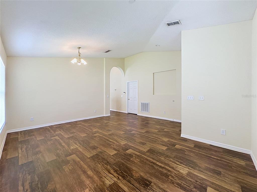 An empty room with light-colored walls, wood-look flooring, a vaulted ceiling, and a chandelier — 3066 EAGLE CROSSING DR, KISSIMMEE, FL