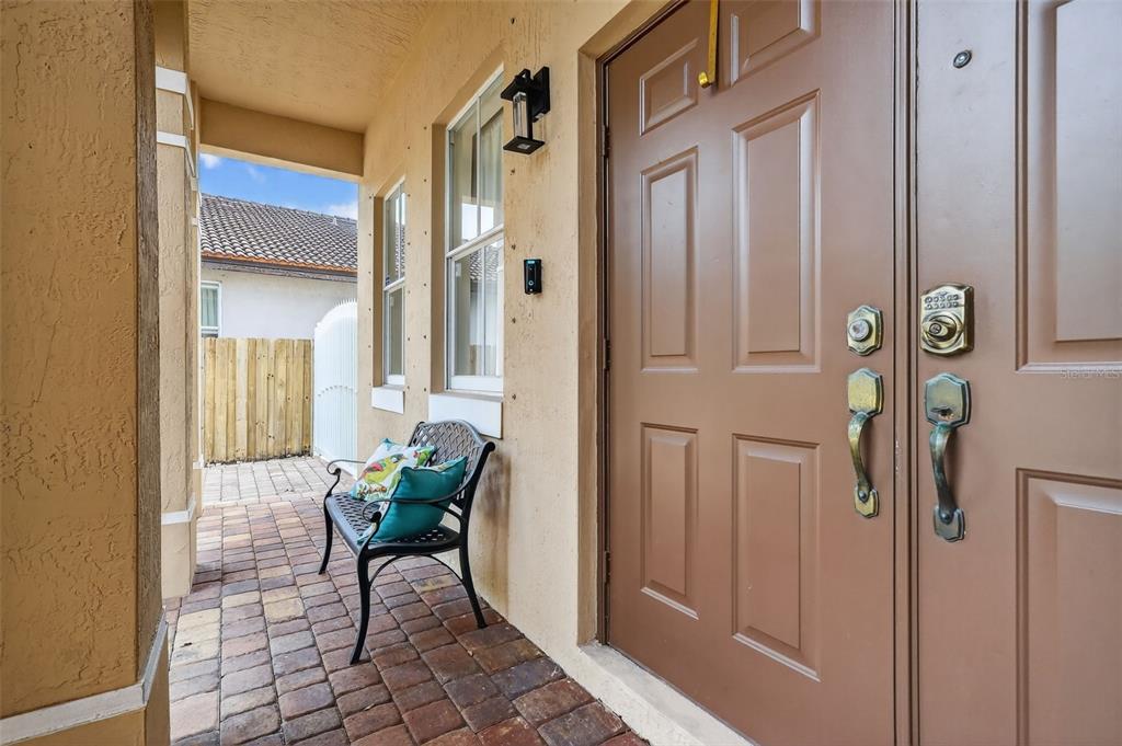 A brown front door with a keypad lock sits beside a bench on a paved porch — 15144 SW 20TH STREET, MIAMI, FL