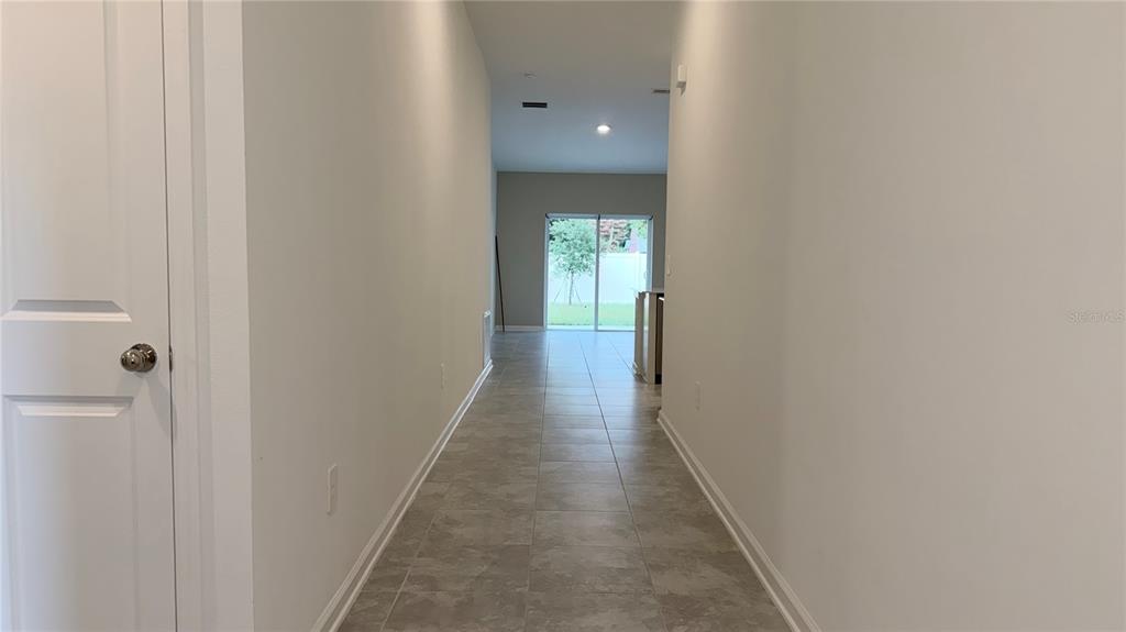 A hallway with light-colored tile flooring leads toward a sliding glass door to the backyard — 1129 DEEPWATER CIRCLE, EAGLE LAKE, FL
