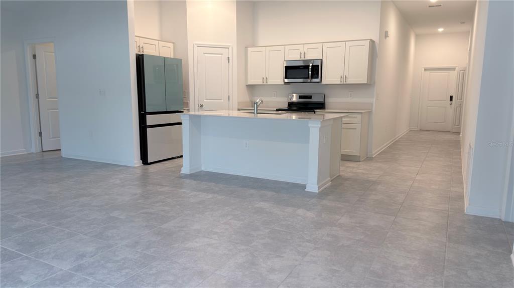 A kitchen with white cabinets, a central island, stainless steel appliances, and gray tiled flooring — 1129 DEEPWATER CIRCLE, EAGLE LAKE, FL