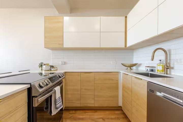 A modern kitchen features white countertops, light wood-toned cabinetry, stainless steel appliances, and bar seating — DR BEACH VILLAGE UNIT 148, HUMACAO, PR