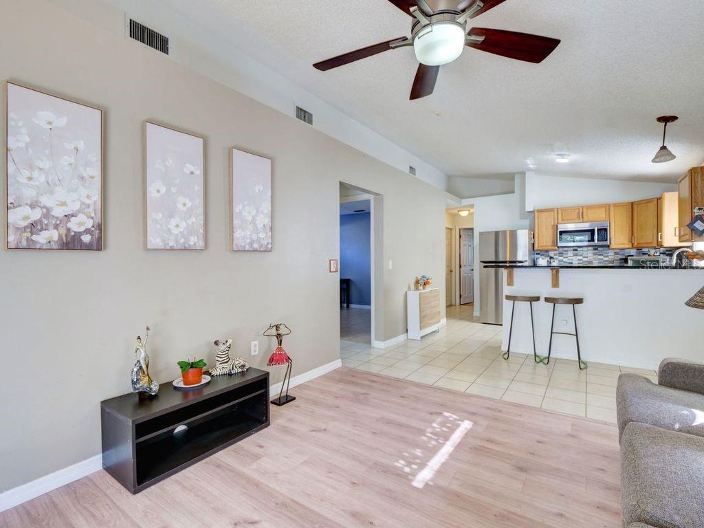 A living room with light wood-look flooring opens to a kitchen with a breakfast bar — 1012 VISTA PALMA WAY, ORLANDO, FL