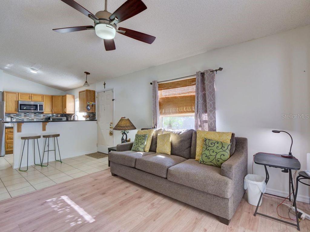 A living room with a gray sofa, light wood-look flooring, and an open kitchen area — 1012 VISTA PALMA WAY, ORLANDO, FL