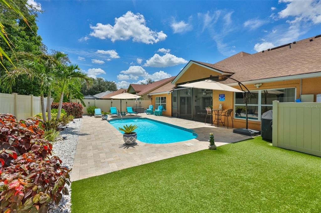 A backyard features a swimming pool, patio furniture, a tan house, and artificial turf — 7613 NOTTINGHILL SKY DRIVE, APOLLO BEACH, FL