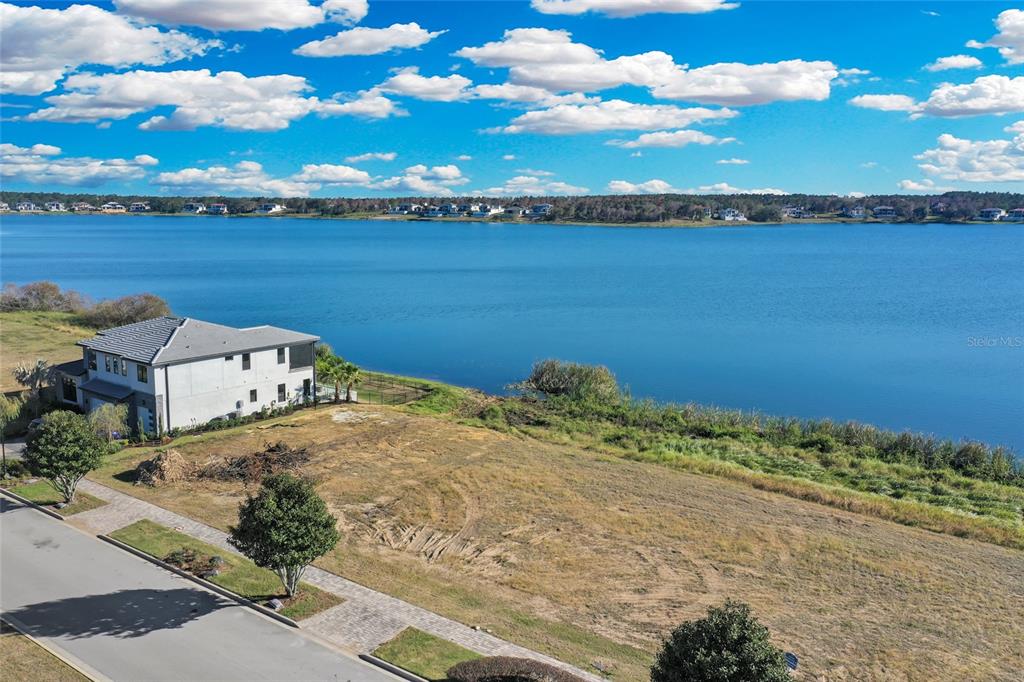 An aerial view shows a vacant waterfront lot next to a modern two-story house — 16626 BOLSENA DRIVE, BELLA COLLINA, FL