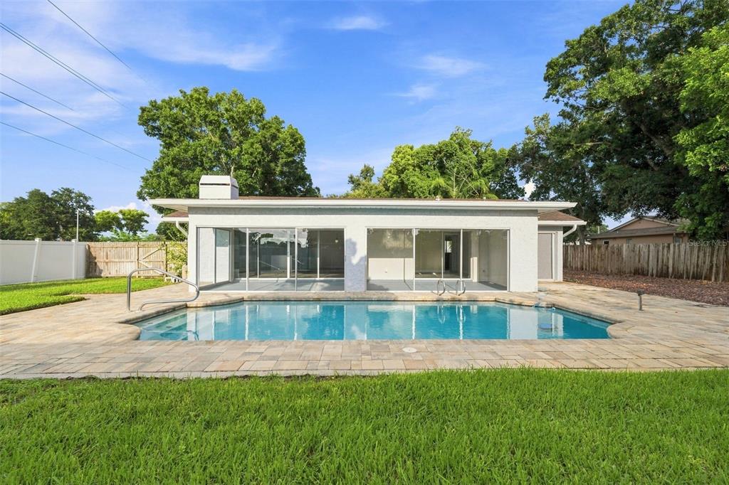 A backyard features a rectangular swimming pool with a paved deck and a white house — 3276 FOX HILL DRIVE, CLEARWATER, FL
