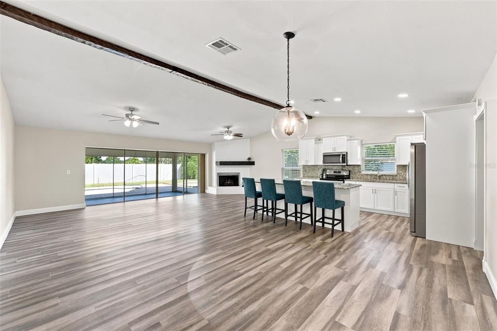 An open-concept living area features a kitchen with white cabinets, a fireplace, and wood-look flooring — 3276 FOX HILL DRIVE, CLEARWATER, FL