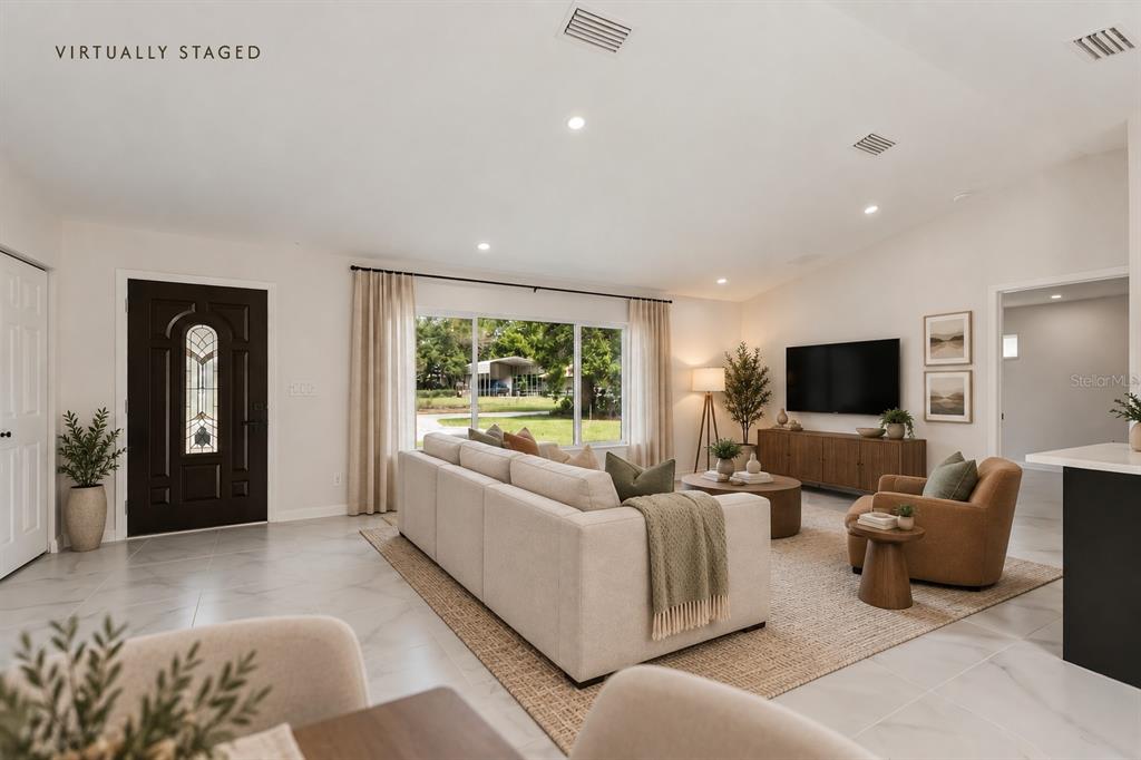 A bright, open-concept living area features white marble-look tile flooring and a dark front door — 2544 N ARROWHEAD ROAD, AVON PARK, FL