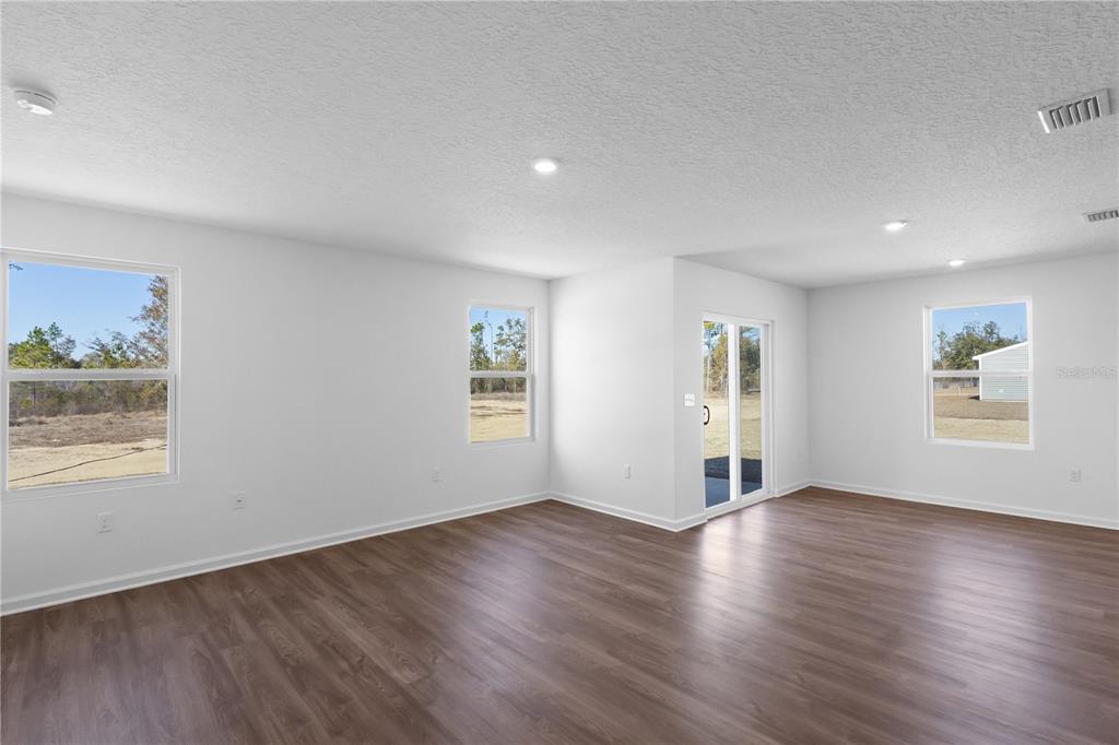 An empty living room with white walls, wood-look flooring, recessed lighting, and sliding glass doors — 14288 NW 162ND PLACE, ALACHUA, FL