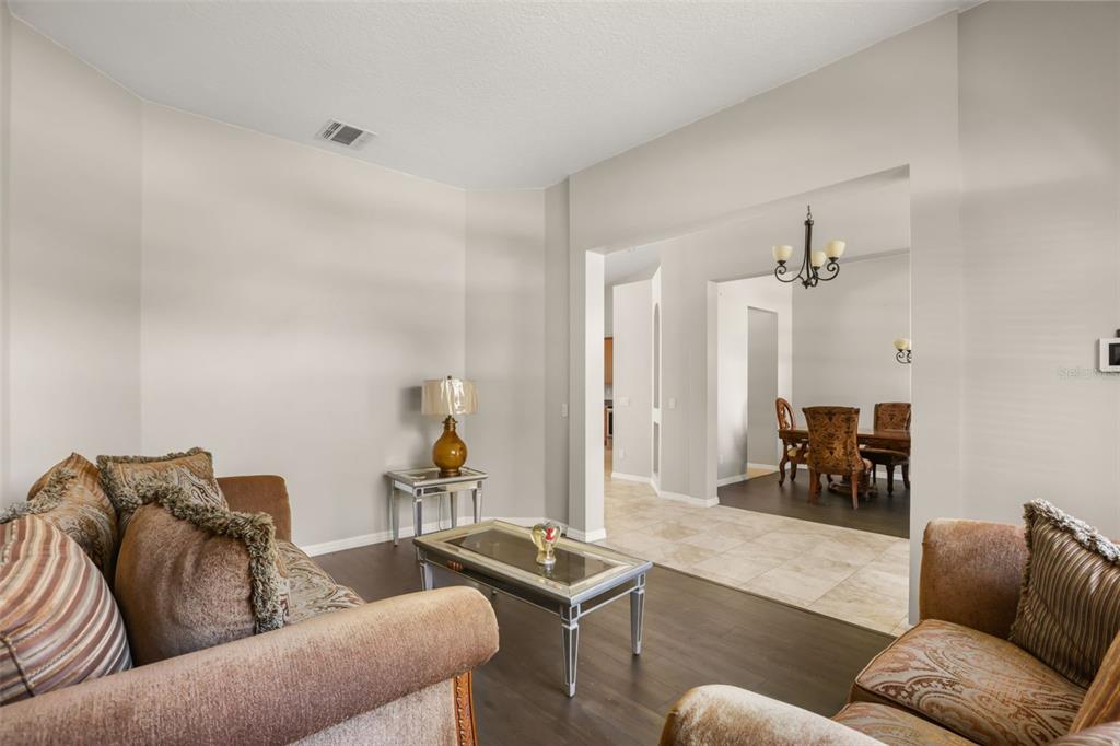 A living room with dark wood floors opens into a dining area with tile flooring — 3451 PLAYERS POINT LOOP, APOPKA, FL