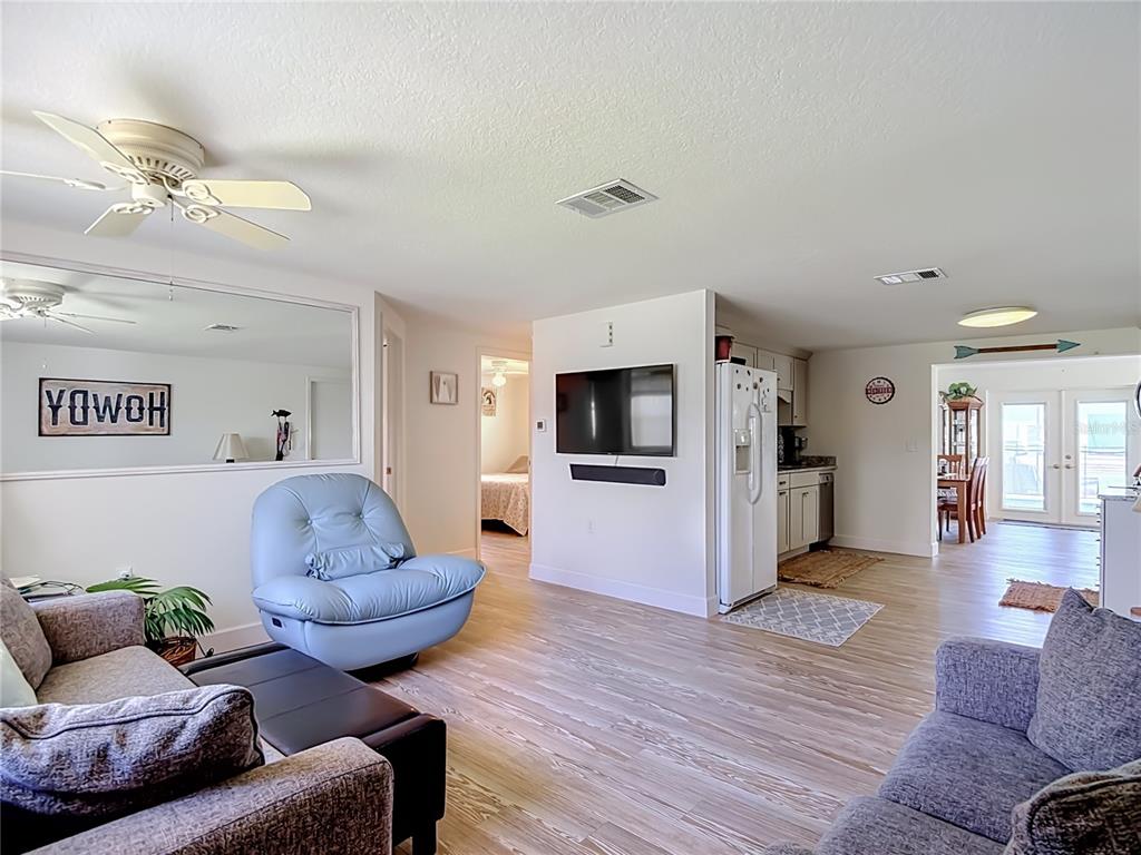 A living room with light wood flooring, a blue armchair, and an open-concept kitchen — 7629 HATTERAS DRIVE, HUDSON, FL