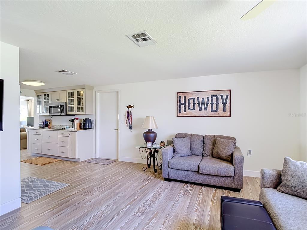 A living room with wood-look flooring, a gray loveseat, and a kitchen in the background — 7629 HATTERAS DRIVE, HUDSON, FL