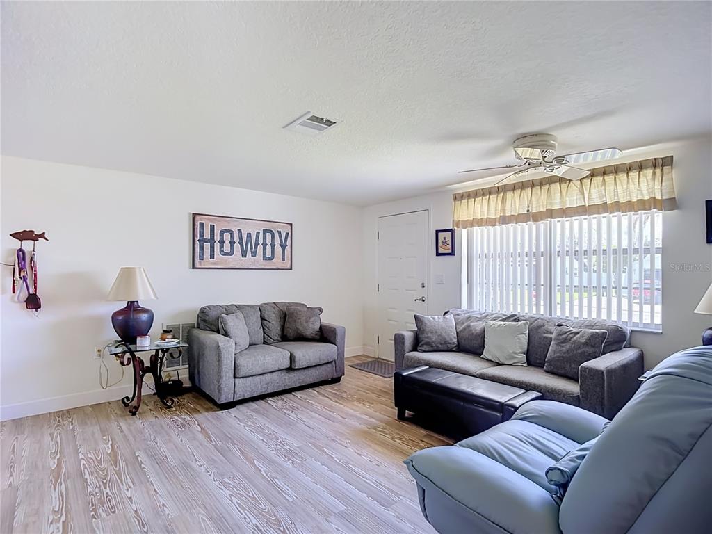 A living room features light wood-look flooring, two gray sofas, and a blue recliner — 7629 HATTERAS DRIVE, HUDSON, FL