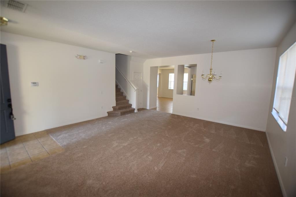 A dining area with a wooden table and chairs sits adjacent to a carpeted living room — 622 ALFANI STREET, DAVENPORT, FL
