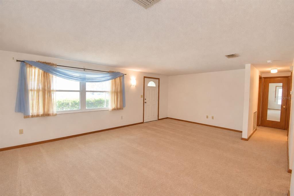 An empty living room features beige carpeting, white walls, a large window, and two doors — 2521 MCCRANIE PLACE, LAKELAND, FL