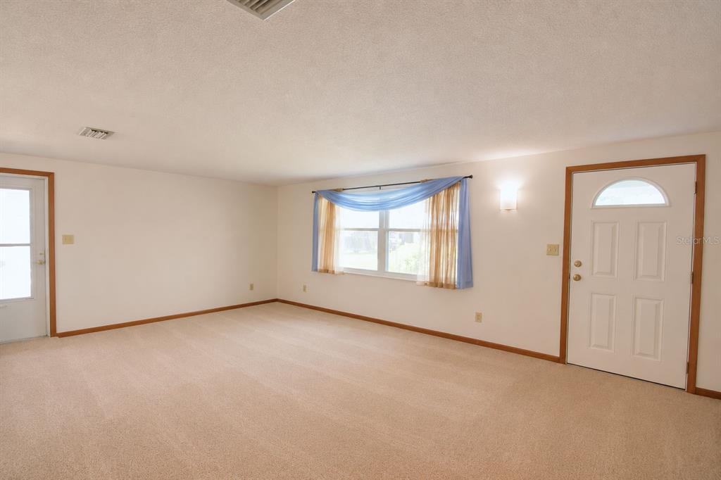 An empty living room features beige carpeting, white walls, a window with curtains, and two doors — 2521 MCCRANIE PLACE, LAKELAND, FL