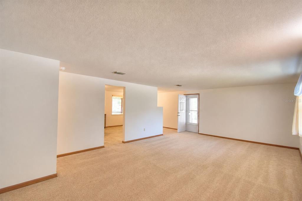 An empty living room with beige carpet, white walls, and a doorway leading to another room — 2521 MCCRANIE PLACE, LAKELAND, FL